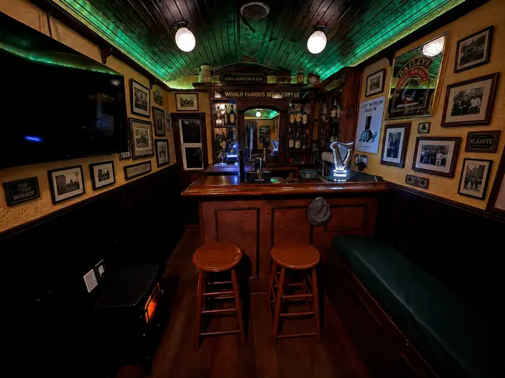 Inside The Síbín — the bar, stools and snug bench under the green-lit ceiling